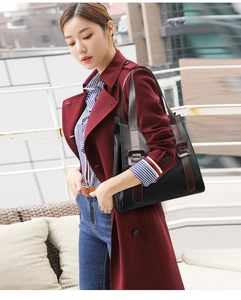 Close-up of black leather tote bag with brown straps styled with a long wine red coat