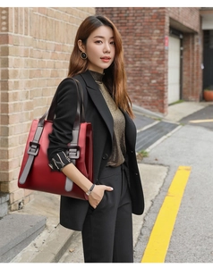 Close-up of red leather tote bag with gray strap detailing and decorative buckle