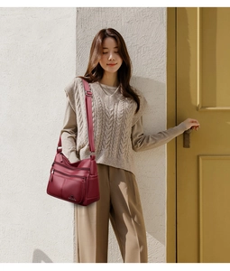 Detail view of burgundy leather shoulder bag featuring multi-zipper pockets and long strap