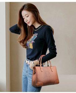 Detailansicht der orangefarbenen Damenhandtasche mit Straußenmuster am Modell