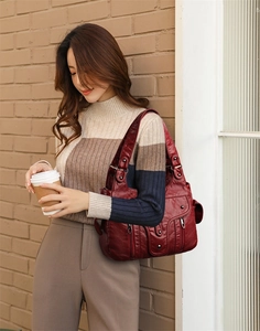 Deep red soft leather tote bag with functional zippers shown on woman's shoulder outdoors