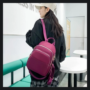 Vue latérale d'un sac à dos en nylon violet avec fermetures dorées porté par un modèle