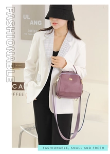 Dettaglio di piccola borsa a tracolla viola in nylon con zip dorata e targhetta metallica