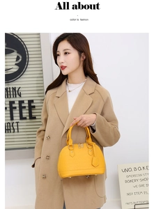 Close-up of a yellow shell handbag with crocodile texture held by a model in a camel coat