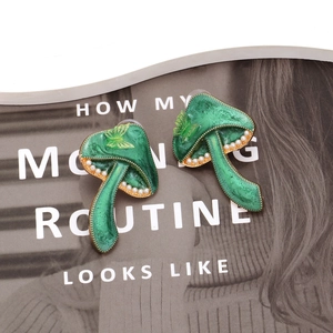 Green mushroom earrings with white pearls and gold butterfly detail on a magazine