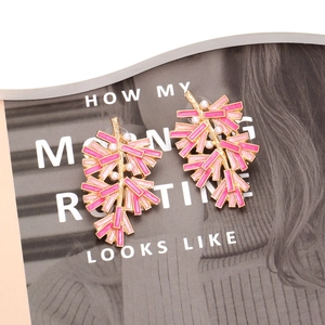 Artistic gold leaf earrings with pink enamel modules and white pearls on a fashion magazine