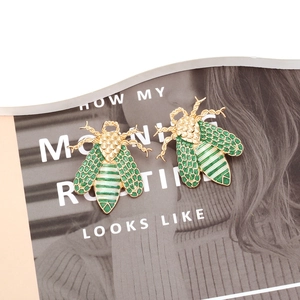 Cute enamel bee stud earrings with gold plating and green texture on magazine background