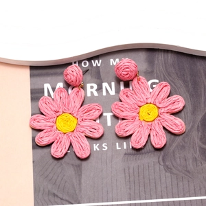 Detailed macro view of pink and yellow raffia woven flower earrings with handmade texture