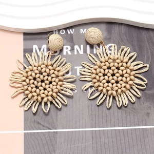 Handmade Bohemian raffia sunflower drop earrings with beaded center on artistic backdrop