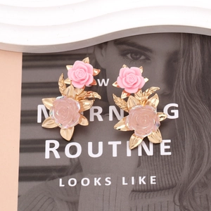 Vintage floral resin earrings with pink roses and gold leaf detail on magazine background
