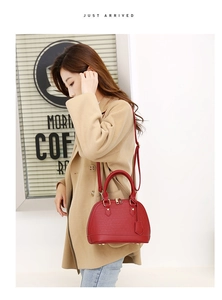 Close-up of wine red shell handbag with crocodile texture worn over a beige coat