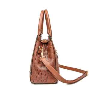 Braune Handtasche mit Krokodilprägung, Goldbeschlägen und verstellbarem Riemen auf Weiß