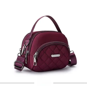 Dettaglio della borsa in nylon trapuntato bordeaux con cerniere multiple e targa argento