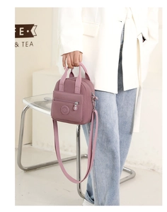 Detail of the mauve nylon crossbody bag featuring a round logo patch and zip pockets