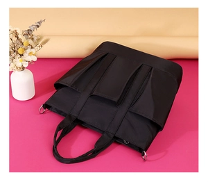 Detail of black nylon tote bag featuring external pockets and metal D-ring for straps