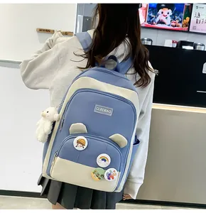 Detail of blue and beige student backpack featuring plush bear and cartoon badges