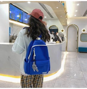 Sac à dos bleu en nylon montrant la poche latérale et le pendentif à damier de profil