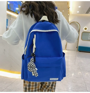 Détail d'un sac à dos en nylon bleu avec zips blancs et pendentif damier dans un centre