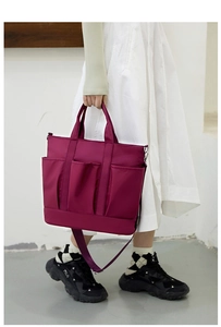 Detail of burgundy nylon tote bag featuring three front pockets and adjustable strap