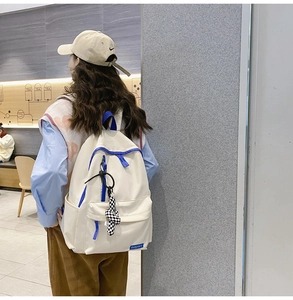 Détail d'un sac à dos blanc en nylon avec zips bleus contrastés et pendentif peluche