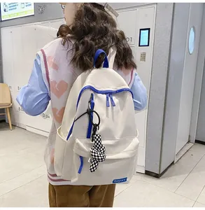 Détail d'un sac à dos blanc en nylon avec bordure bleue et breloque damier pour étudiant