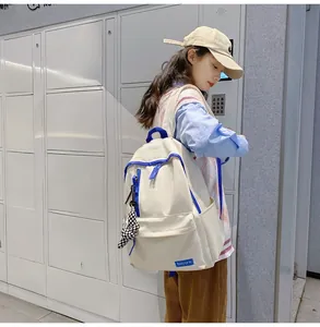 Détail d'un sac à dos en nylon beige avec liserés bleus et breloque à carreaux