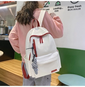 Détail du sac à dos en nylon blanc avec fermetures rouges contrastées et breloque à carreaux