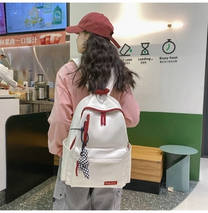 Détail du sac à dos en nylon blanc avec fermetures éclair rouges et pendentif à carreaux