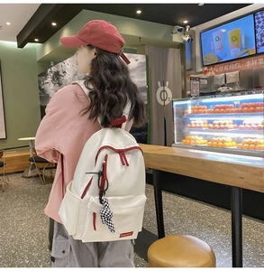 Détail de sac à dos en nylon crème avec fermetures éclair rouges sur modèle féminin