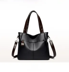Front view of black pebble textured trapezoid handbag with brown leather handles and kangaroo logo
