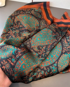 Detail of silk satin scarf featuring orange paisley patterns and smooth glossy texture