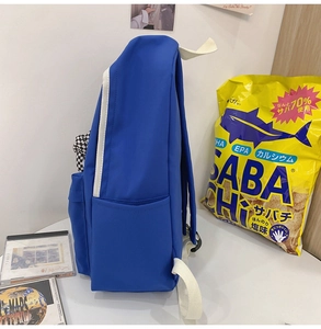 Détail du sac à dos bleu en nylon avec bretelles blanches et porte-clé à damier latéral