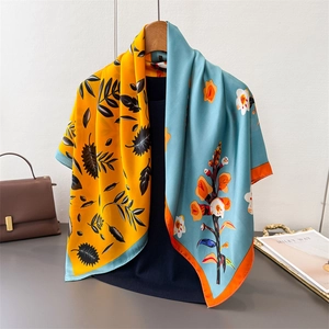 Detail of silk-feel scarf with yellow palm and blue floral prints on a wooden hanger