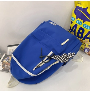 Détail du sac à dos en nylon bleu roi avec liseré blanc et pendentif en damier noir