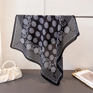 Elegant black and white daisy pattern silk scarf displayed with pearl handbag and tray