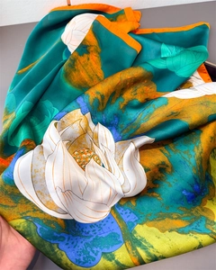Detail of silk-like scarf featuring orange lotus print on a turquoise background