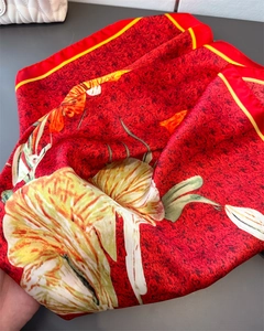 Detail of red faux silk scarf featuring lily print and yellow border edges