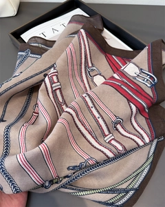 Detailstruktur des Seidenschals mit Reitsport-Zaumzeug-Druck und Ketten in warmen Tönen