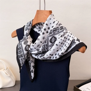 Dettaglio di un foulard di seta paisley bianco e nero annodato su una maglia blu
