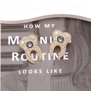 Détails de boucles d'oreilles dents dorées avec cristaux et perle sur un magazine