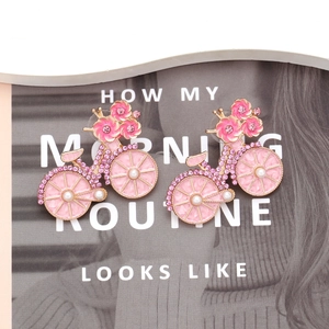 Elegant pink enamel bicycle earrings with gold plating, rhinestones, and pearls on magazine