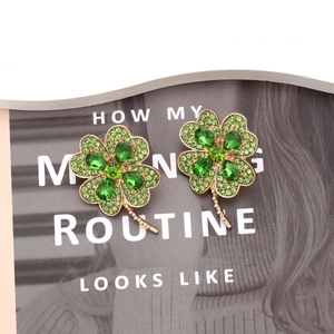 Détail de boucles d'oreilles trèfle à quatre feuilles dorées et cristaux verts sur revue
