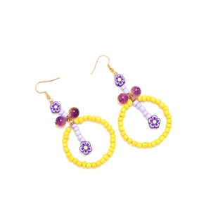 Détail de boucles d'oreilles bohèmes en perles jaunes avec des breloques de fleurs mauves