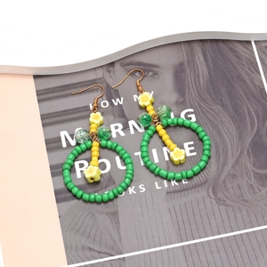 Vue détaillée des boucles d'oreilles en perles vertes faites main avec fleurs jaunes sur magazine