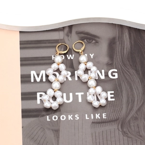 Baroque pearl earrings in elegant S-shape curve with gold hoops on magazine background
