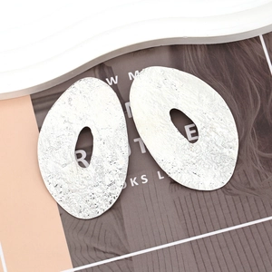Detailed macro view of large oval earrings with hammered silver metal texture and geometric cut-out