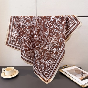 Brown silk-like square scarf with white paisley pattern draped on a stand