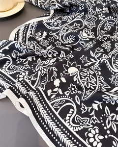 Detail shot of black and white paisley silk scarf with fine stitched edges on a flat surface