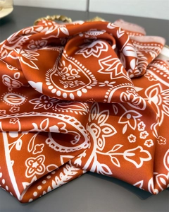 Close-up of caramel orange silk-like scarf featuring classic white paisley floral patterns