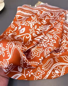 Detail of orange paisley silk-like scarf showing luxury satin texture and fine floral print